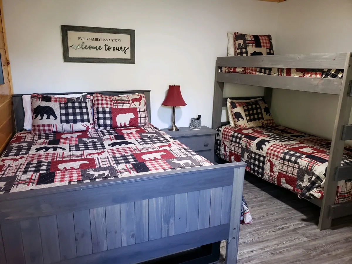 A warm, welcoming bedroom combining a queen bed and a bunk bed, complemented by a bedside lamp and tasteful wall decor. The arrangement is clearly designed for families or groups, offering both comfort and versatility.