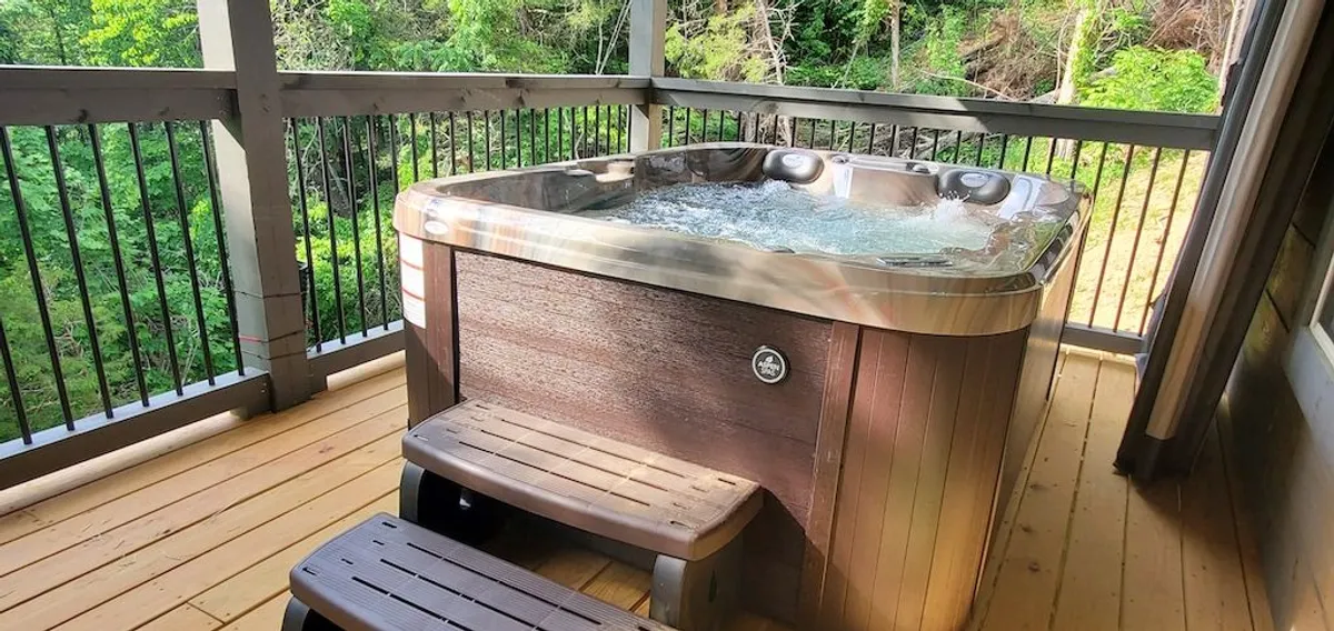 This image captures a hot tub on a wooden deck surrounded by lush greenery. The tranquil setting suggests privacy and invites relaxation. The image hints at opportunities for stargazing from the warm water, enjoying morning coffee, or leisurely afternoons in nature.