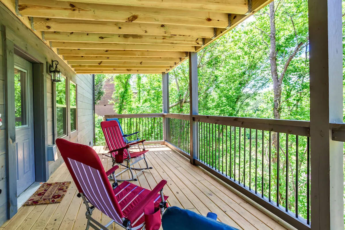 An exterior view of a wooden deck with two red chairs, overlooking abundant greenery. The setup invites guests to relax, read, or simply enjoy the serene surroundings and possibly watch for wildlife.