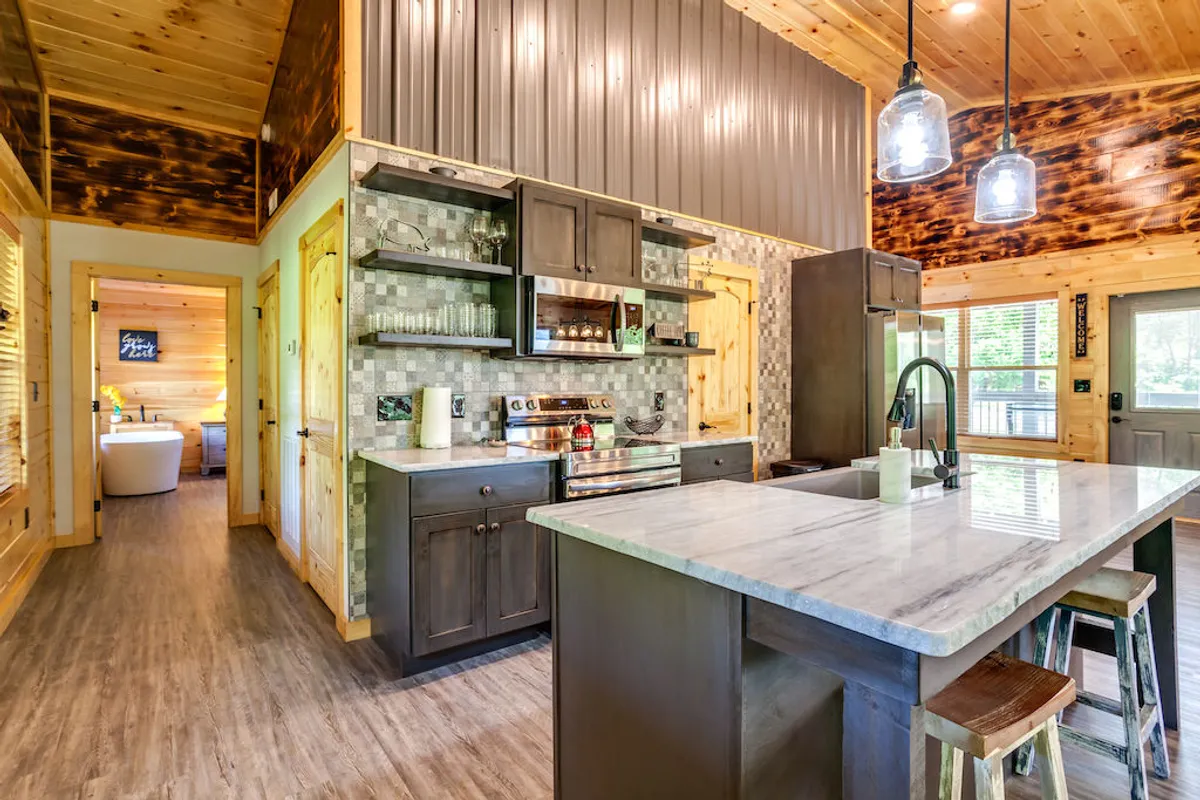 A modern kitchen with a central island, stainless steel appliances, wooden cabinets, and pendant lighting. The inviting layout is designed for meal prep, cooking, and casual gatherings, complemented by thoughtful decor and natural light.