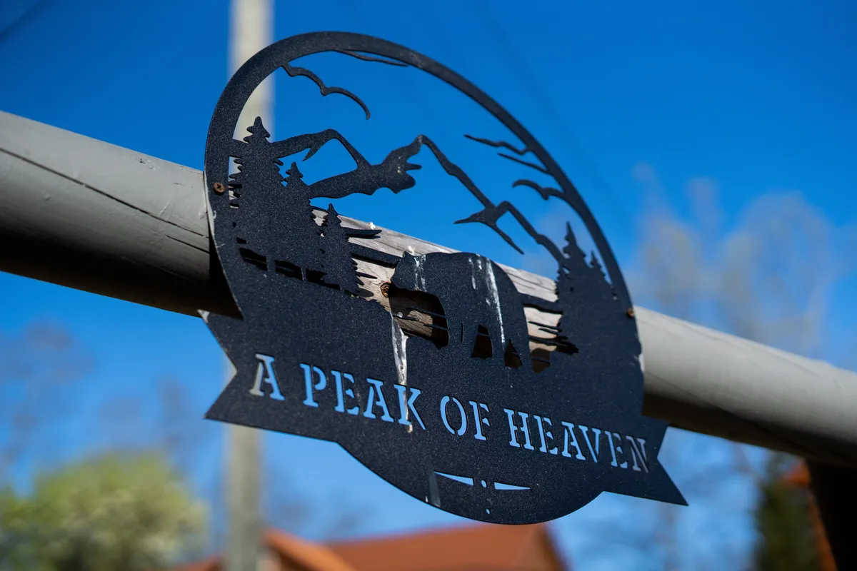 A serene exterior scene featuring a metal sign with a mountain silhouette, flanked by trees and birds in the background. The open landscape and natural elements evoke the spirit of adventure and the nearby Smoky Mountains.