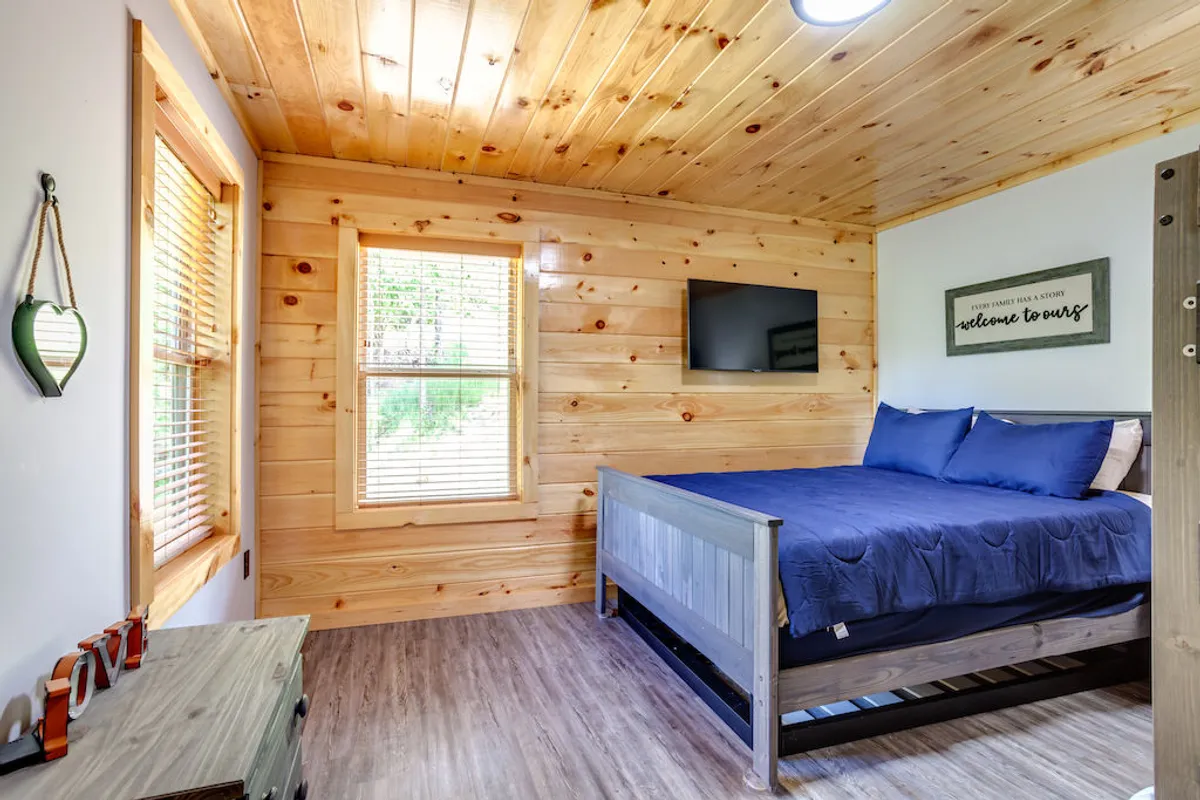 This inviting bedroom features wooden walls that create a cozy cabin feel, a king-sized bed with soft blue bedding, and a smart TV mounted on the wall. A small 'welcome' sign adds a personalized touch, making the space ideal for relaxation and private downtime.