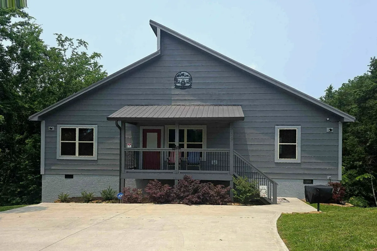 A welcoming exterior shot of the cabin featuring a front porch with a bright red door, comfortable seating, and lush landscaping. The porch is perfect for gathering as a family before or after a day of adventure, and the inviting entry sets the tone for a fun-filled stay.